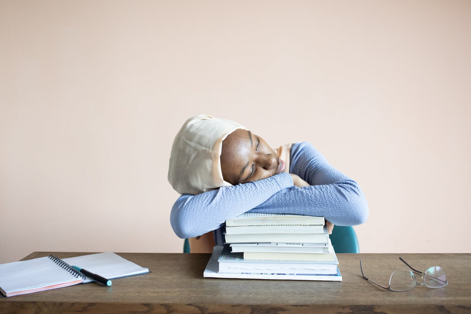 An adult student laying her head on a while of books.