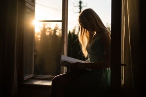 Woman reading on windowsill with sunset in background