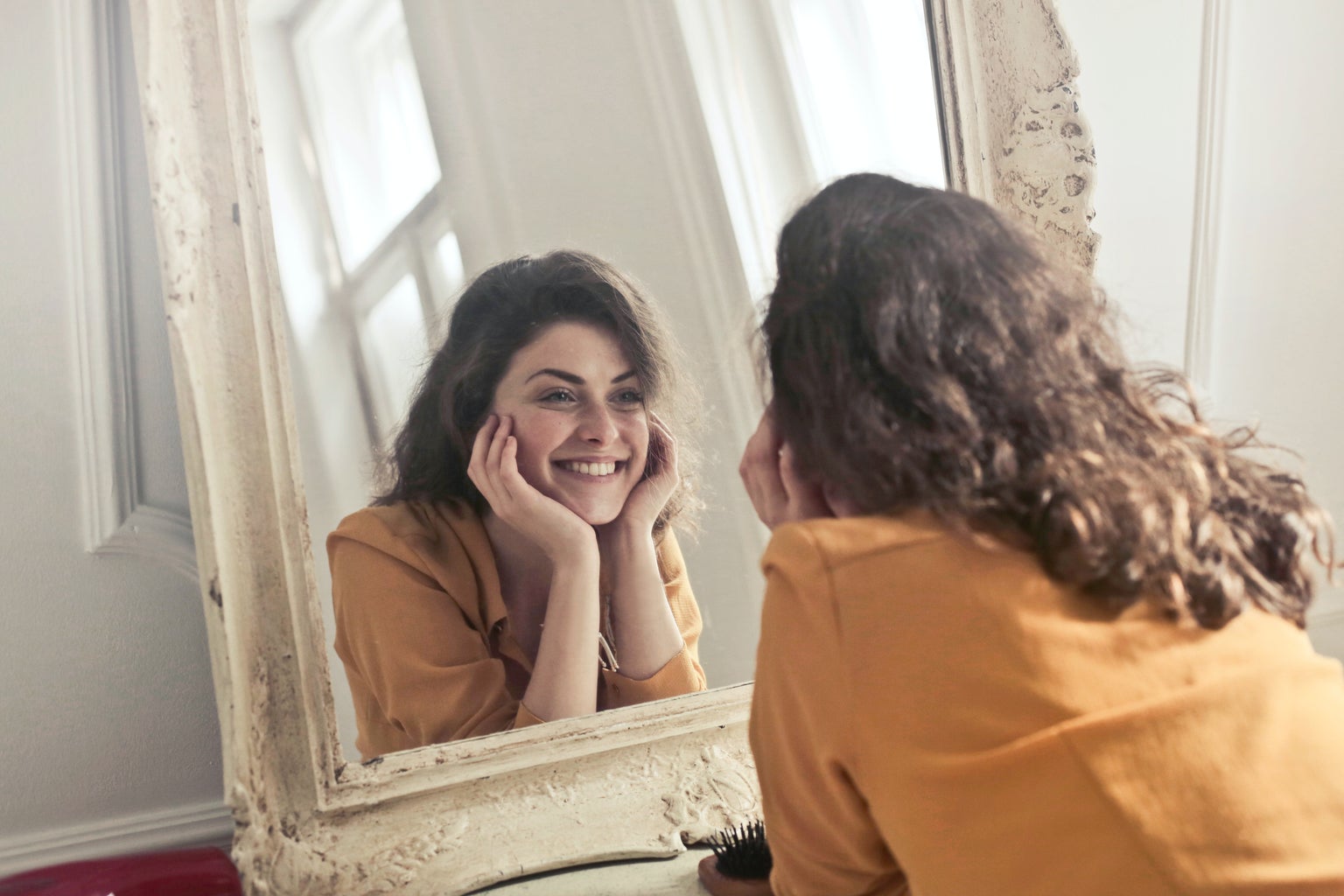 photo of woman looking at herself in a mirror and smiling