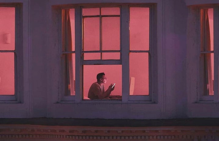 Photo of a man sitting at his desk in a pink-lit room