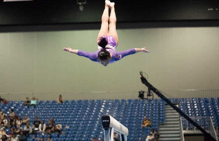 gymnast in a purple leotard performing a mid-air trick over the balance beam