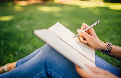 Person sitting on grass writing in journal