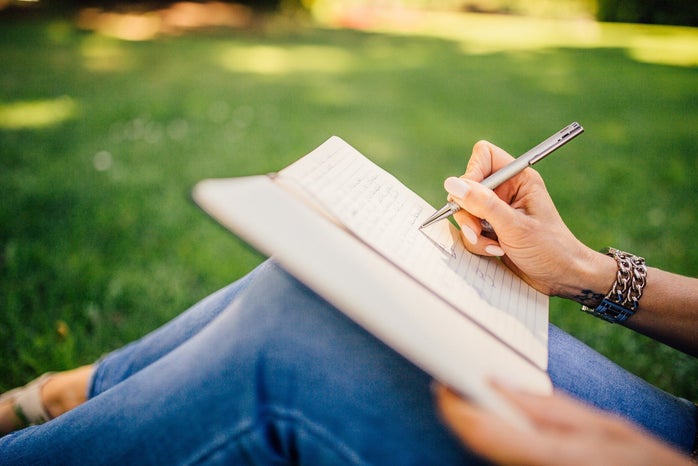 Person sitting on grass writing in journal
