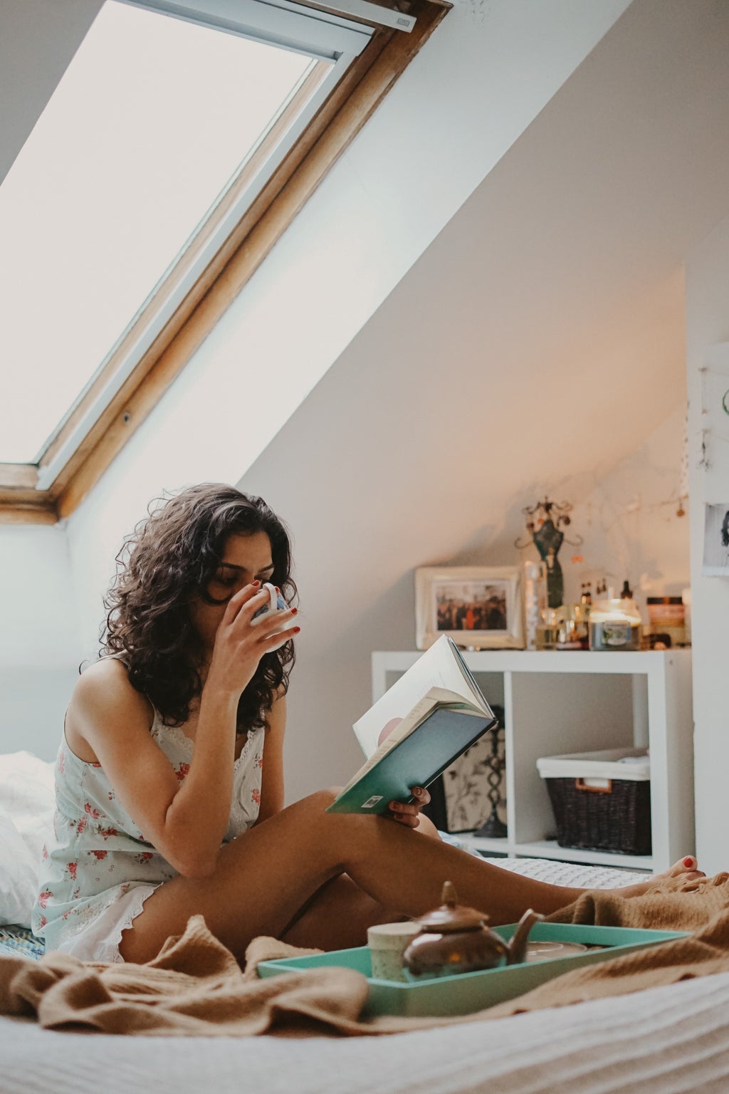 Girl sitting on bed, reading and drinking coffee.