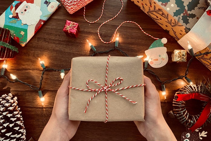 hands holding a wrapped present surrounded by lights and gifts