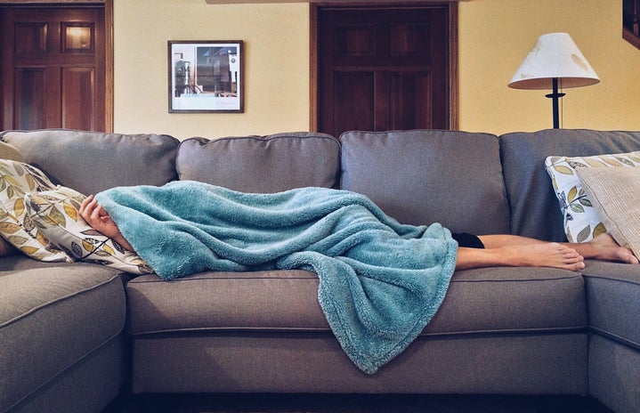 Woman laying down on a couch covered in a blanket.