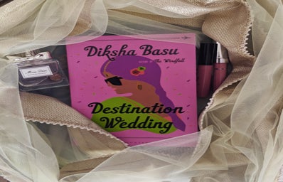 Book Destination Wedding with cloth wrapped around it with fairy lights, a perfume and lipgloss.