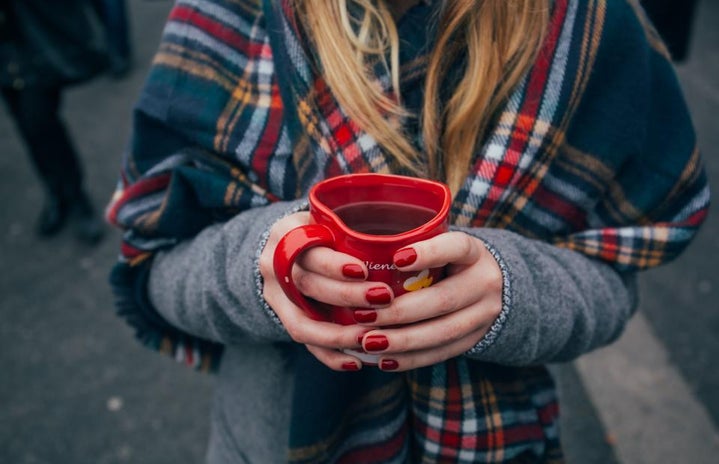 Girl with red manicure holding a red mug. She is wearing a plaid scarf. Fall vibes, cozy.