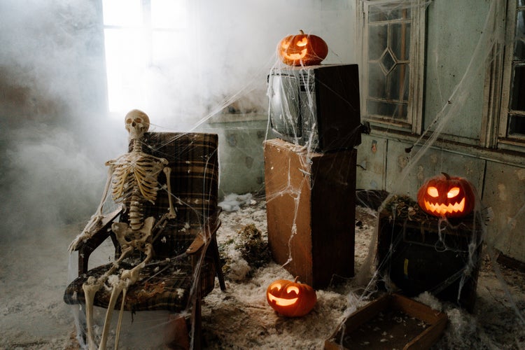 a skeleton in a chair, jack-o-lanterns, and cobwebs.
