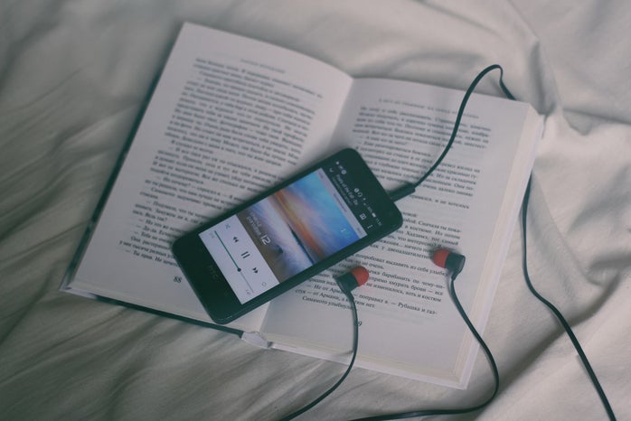 open book placed on white sheets with a phone playing music through headphones