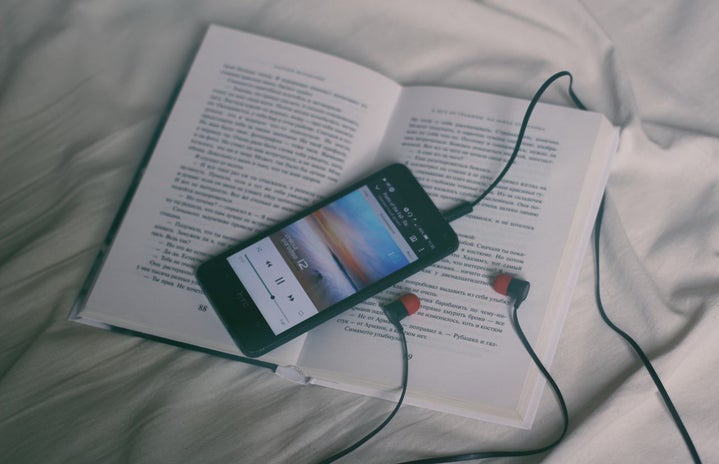 open book placed on white sheets with a phone playing music through headphones