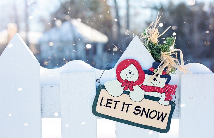a sign that says \"let it snow\" with snowmen are displayed on white fence.