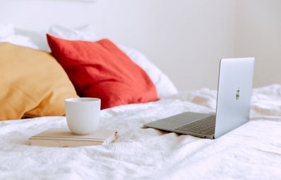 laptop on bed with a mug on top of a book