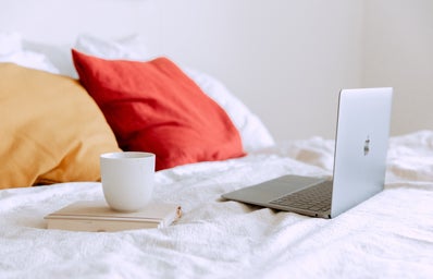 laptop on bed with a mug on top of a book