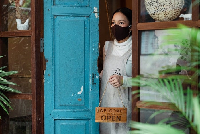 Woman wearing mask holding Open sign by Ketut Subiyanto?width=698&height=466&fit=crop&auto=webp