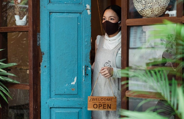 Woman wearing mask holding “Open” sign