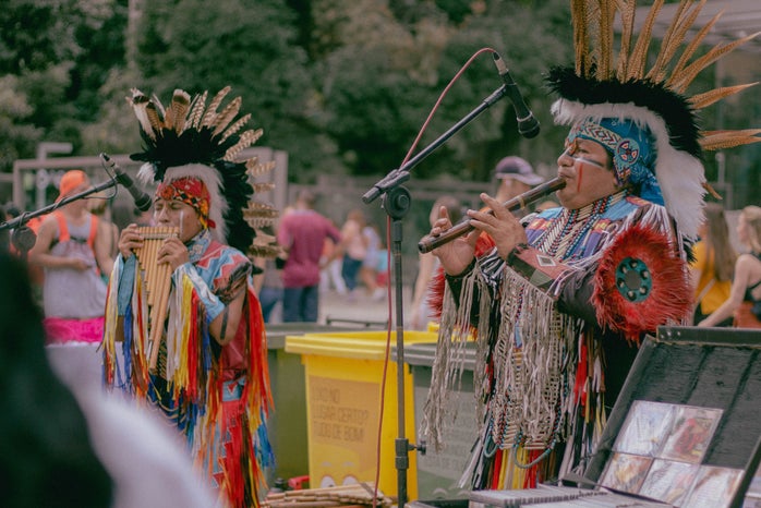 two native americans playing woodwind instruments in traditional clothing