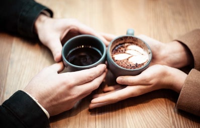 two people holding coffee mugs on table
