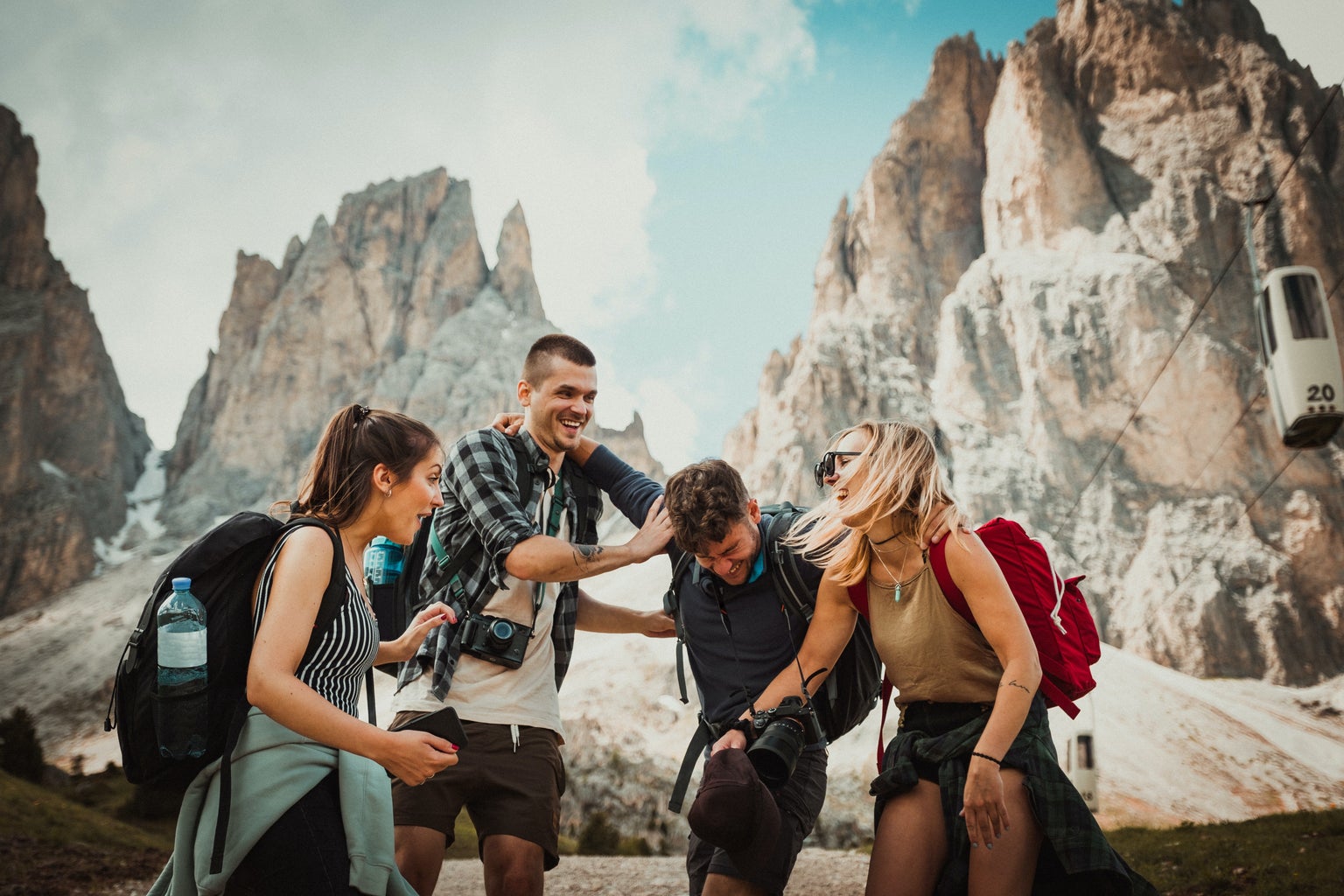 Two men and two women wearing backpacks laughing in front of mountains