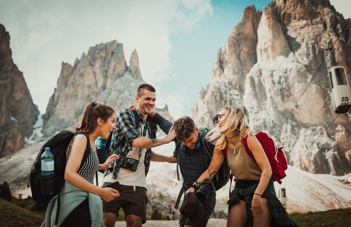 Two men and two women wearing backpacks laughing in front of mountains