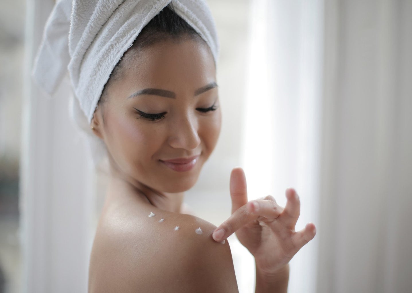 woman with towel on her head using lotion on shoulders