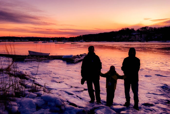 three people standing on frozen lake near boats