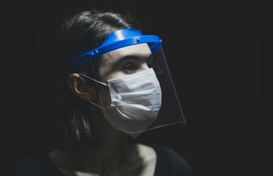 Person with face shield and surgical mask on against black background