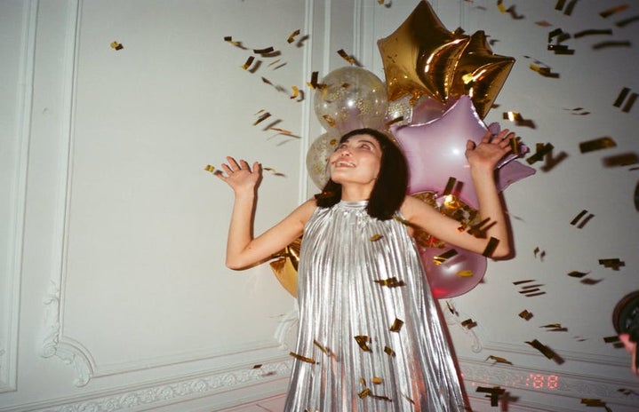 A girl in a silver dress with gold confetti and pink and gold balloons surrounding her