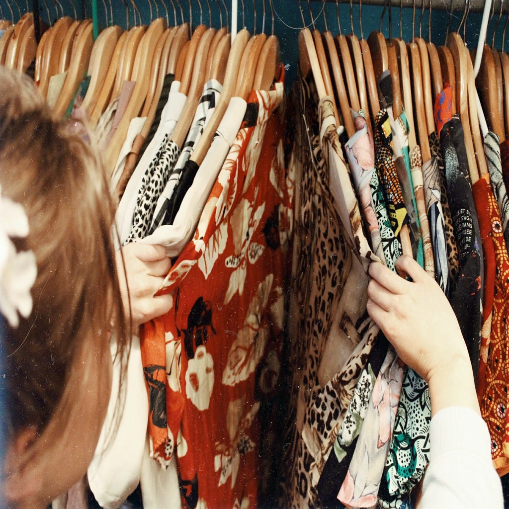 A woman going through some clothes hanging on a closet