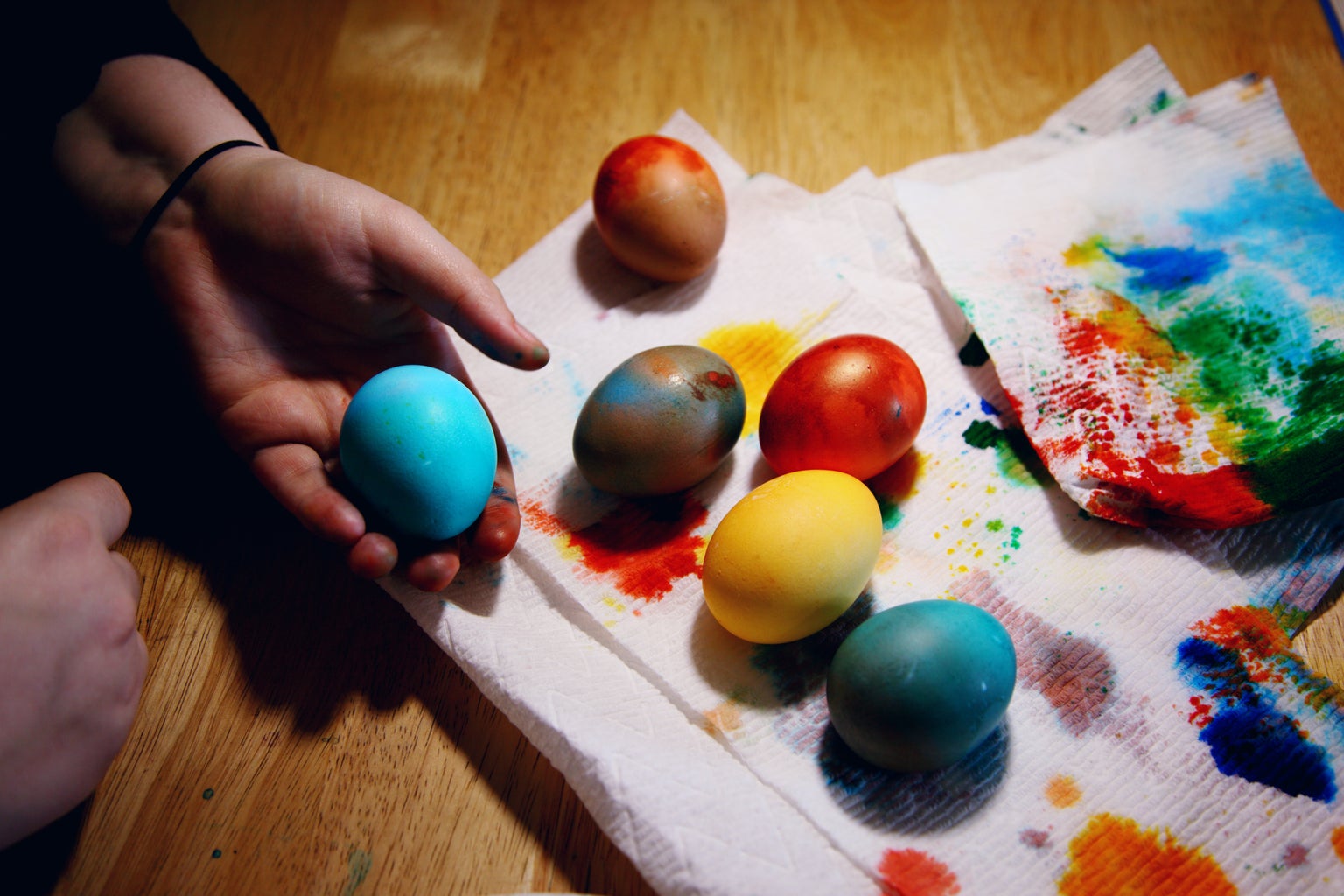 Person holding a blue egg among other colorful eggs on paper towel