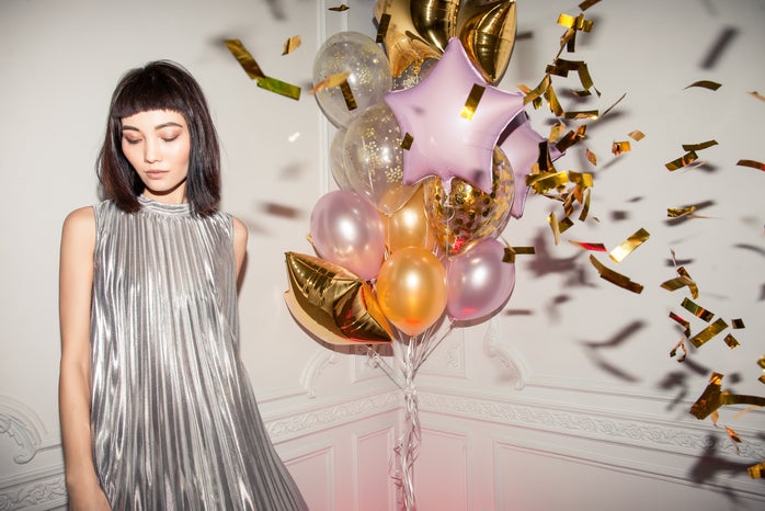 woman wearing a silver pleated dress standing next to balloons