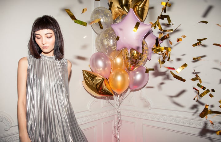 woman wearing a silver pleated dress standing next to balloons