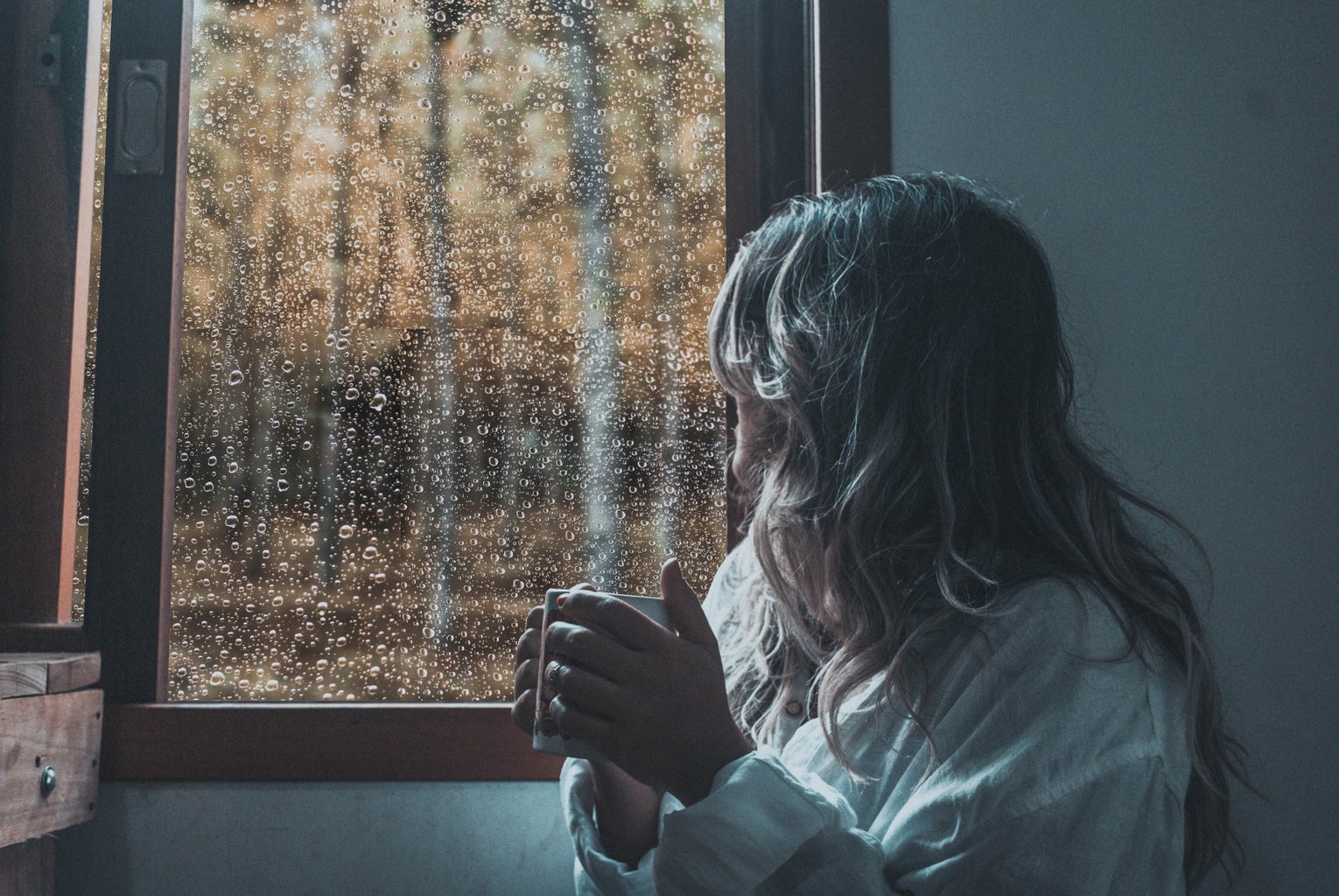 woman in white long-sleeve shirt looking out a rainy window