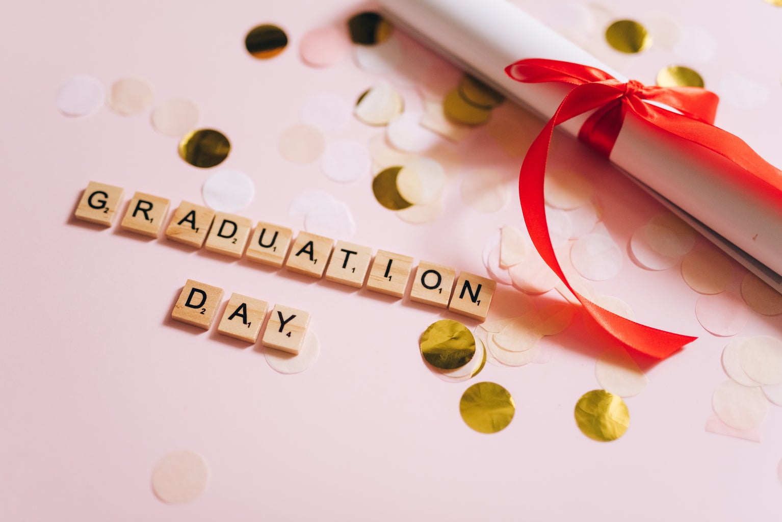 High Angle Shot of Scrabble Tiles spelling out \'Graduation Day\' and a rolled diploma.