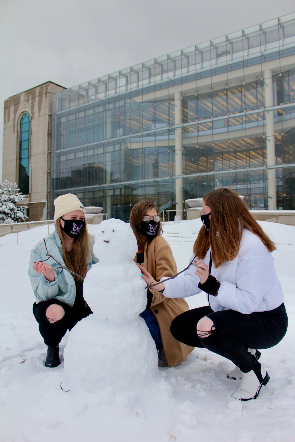 Three women posing with their snowman on campus