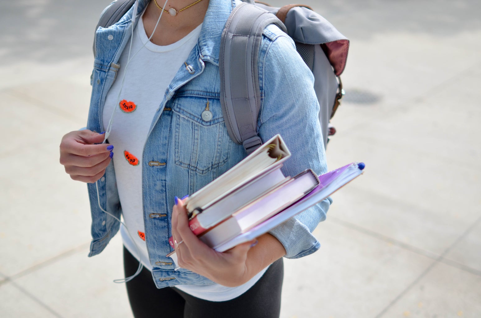 Student listens to music, with books in hand and a denim jacket