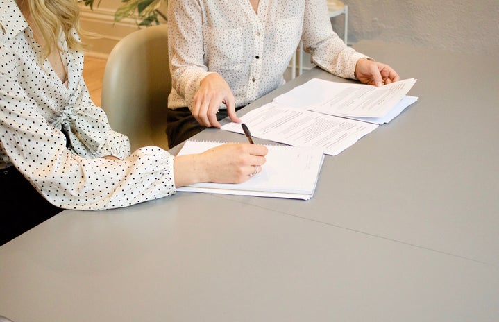 two women sitting at table signing papers