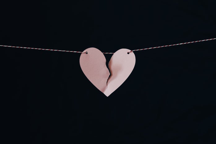 A torn pink paper heart strung on white string with a black background.