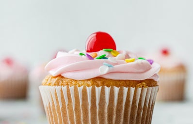 Vanilla cupcake with pink frosting, sprinkles, and a cherry.
