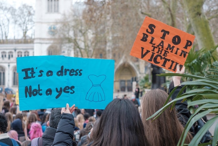 Two signs at a protest. One says \"It\'s a dress not a yes\" and the other \"Stop blaming the victim.\"