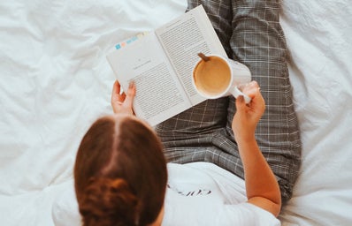 Woman Reading book in bed with coffee