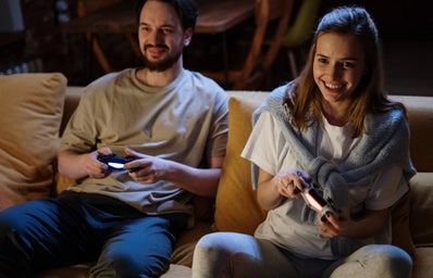 A girl and a guy sitting on a couch and smiling with video game controllers in their hands.