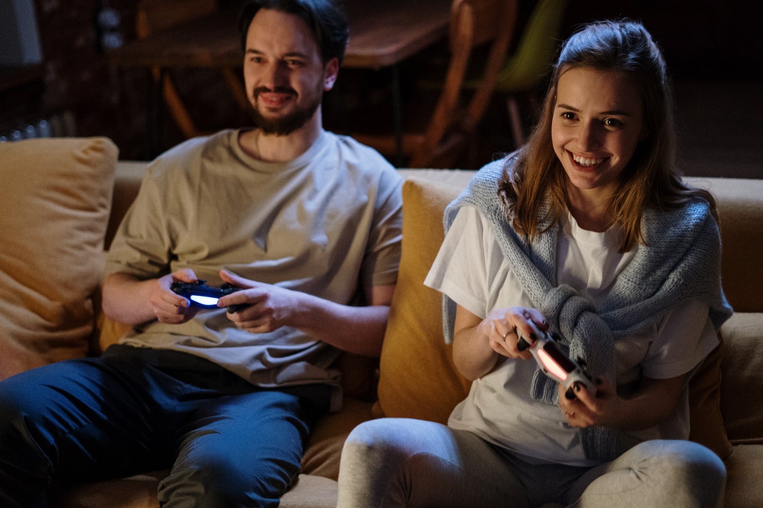 A girl and a guy sitting on a couch and smiling with video game controllers in their hands.