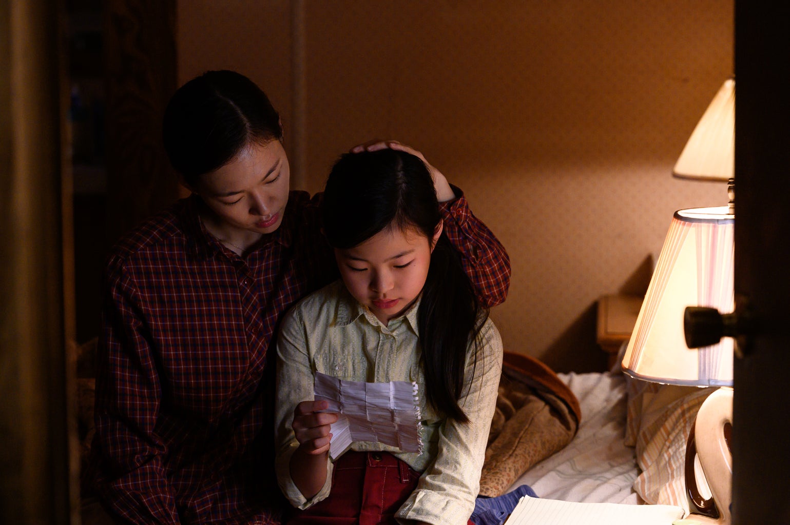 Monica Yi and her daughter Anne sitting on a bed and reading a note together.