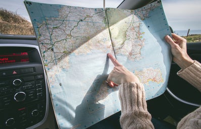 Person pointing at a fold-up map in a car.