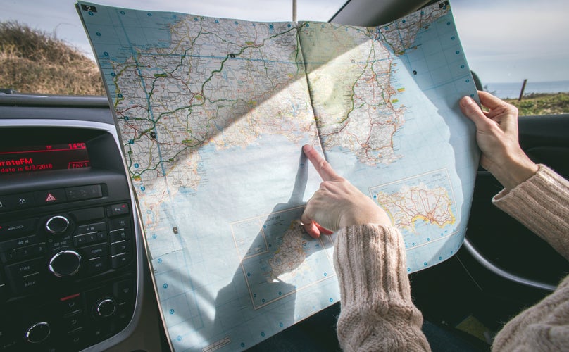 Person pointing at a fold-up map in a car.