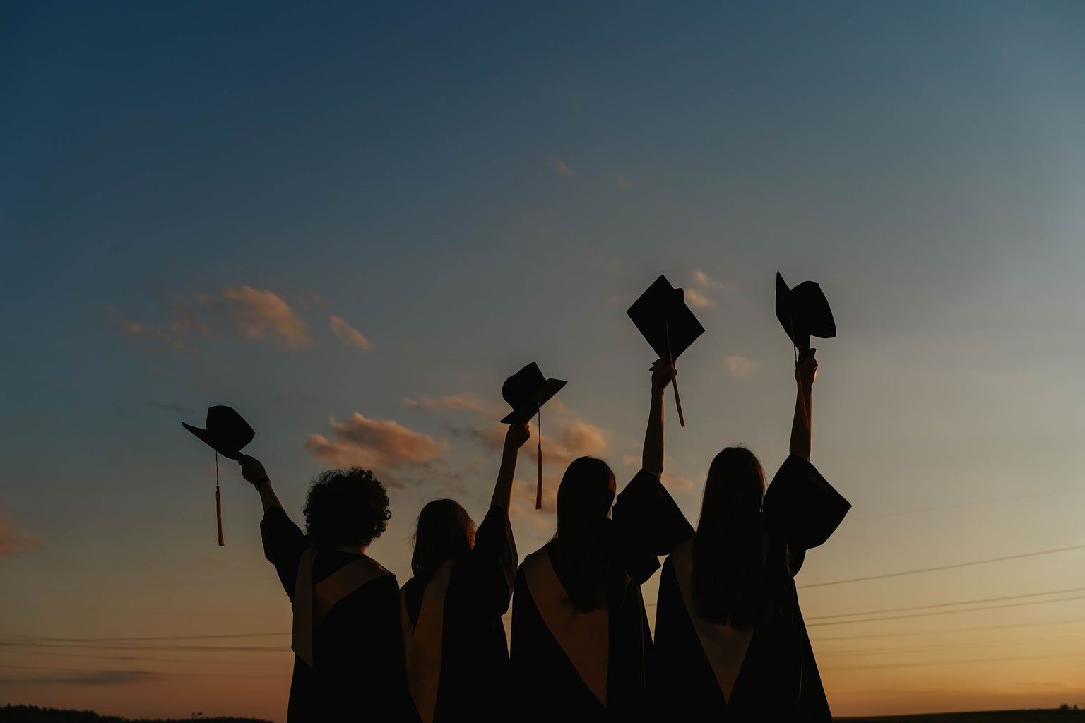 Silhouette of People Raising Their Graduation Hats against a sunset