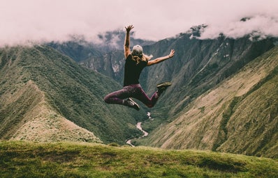 woman jumping in the air in front of green mountains
