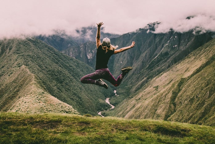 woman jumping in the air in front of green mountains