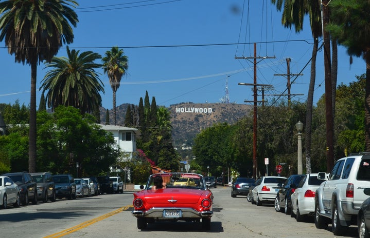 driving in red convertible with Hollywood sign in the distance